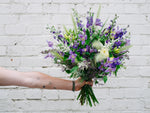 A handed bouquet with purple flowers and green foliage