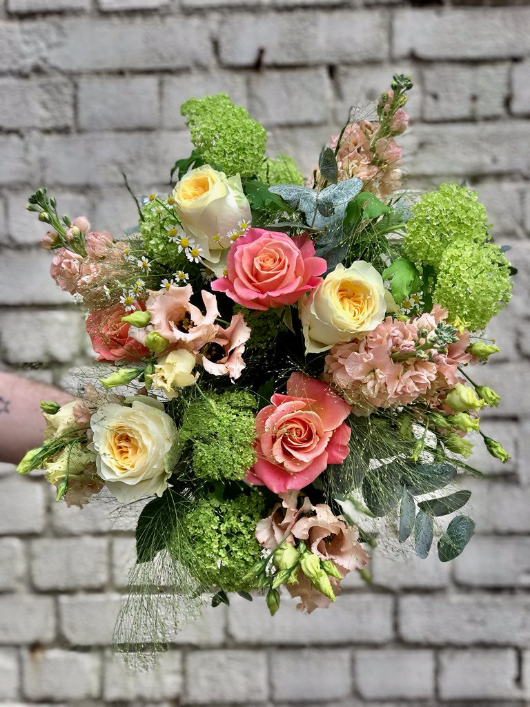 A bouquet with lime green foliage and flowers in shades of coral and lemon