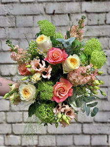 A bouquet with lime green foliage and flowers in shades of coral and lemon